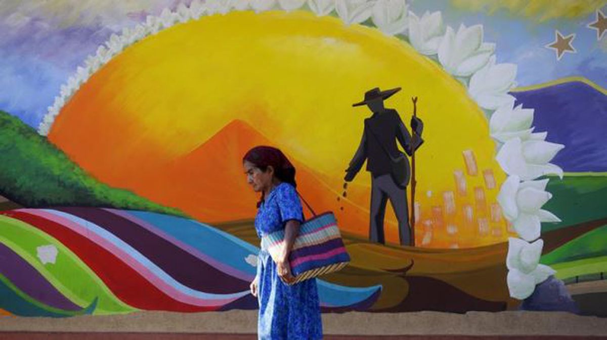 Una mujer camina frente a un mural en San Salvador. Foto: EFE