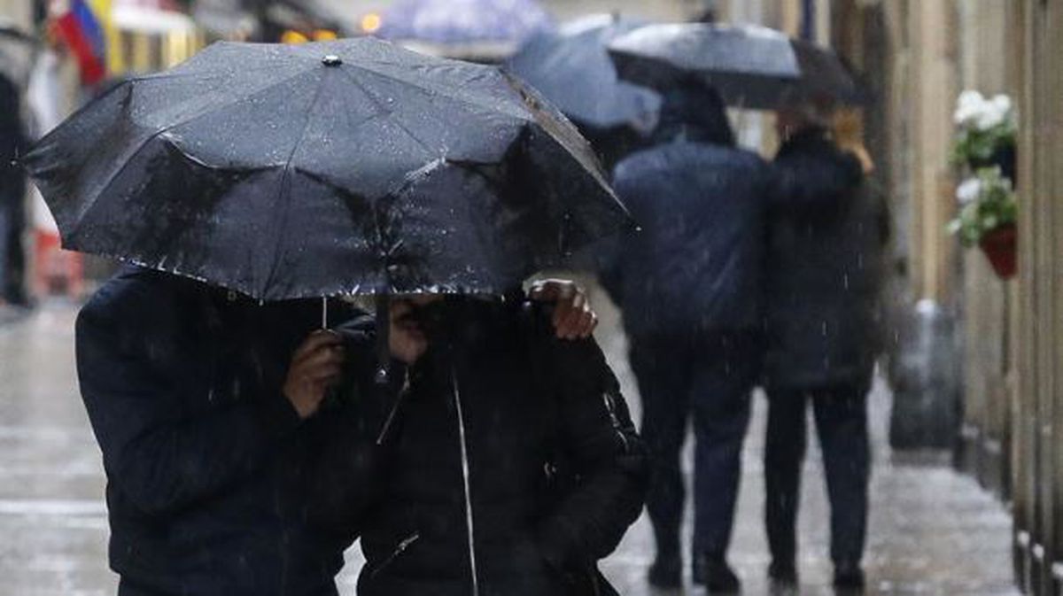 Varias personas se se resguardan de la lluvia bajo el paraguas. Foto de archivo: EFE