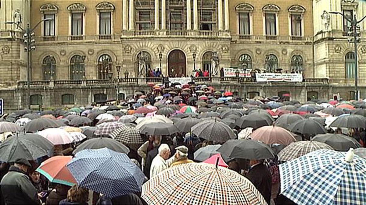 Los pensionistas se concentran en frente al Ayuntamiento de Bilbao bajo la lluvia paraguas en mano.