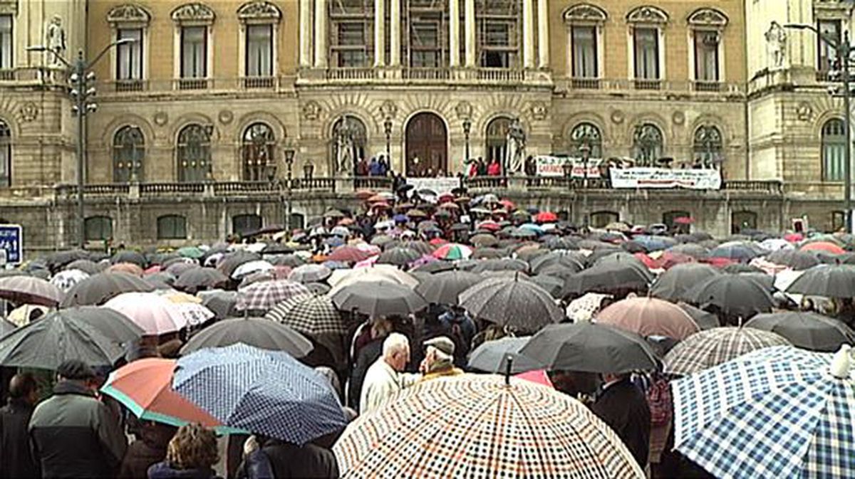 Los pensionistas se concentran en frente al Ayuntamiento de Bilbao bajo la lluvia paraguas en mano.