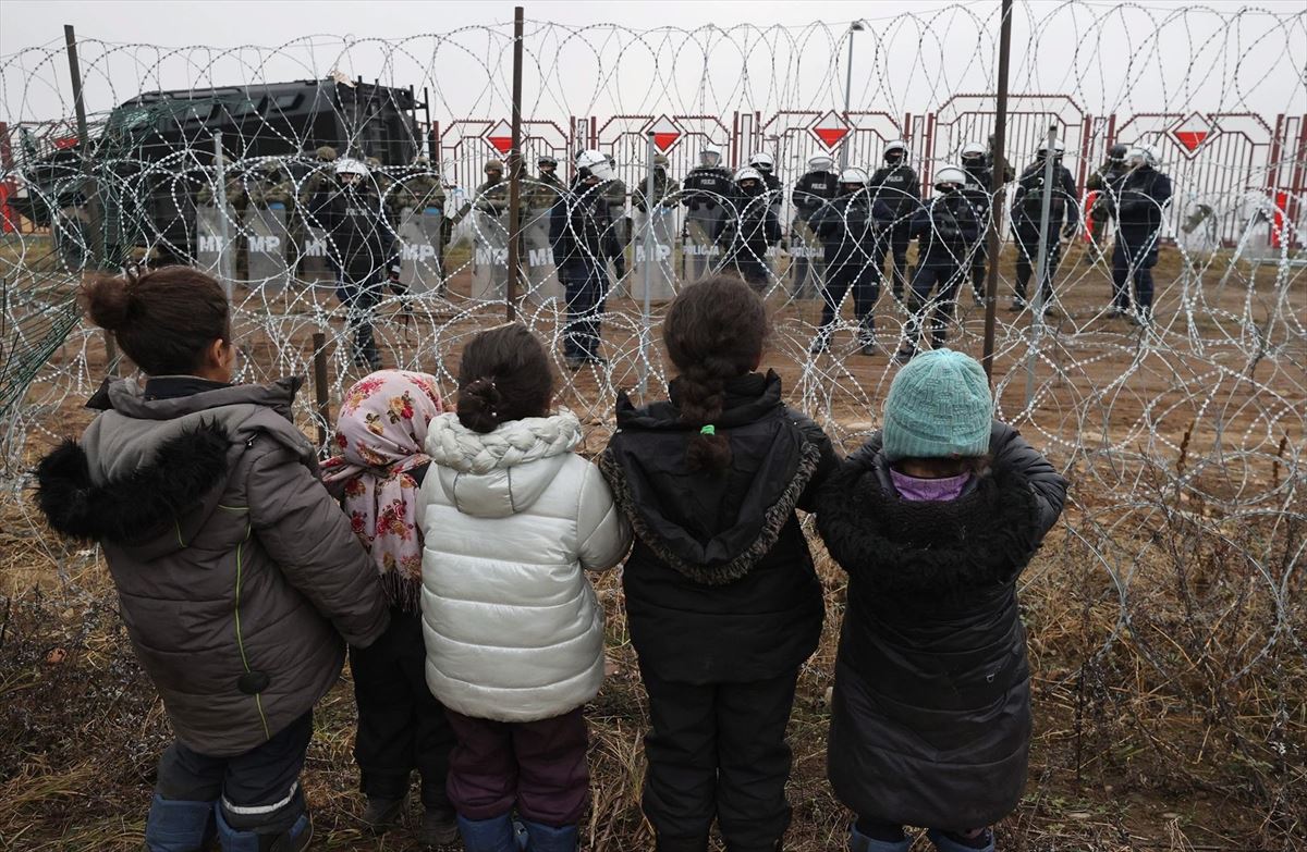 Menores migrantes observan a los policías polacos que vigilan la frontera. Foto: EFE