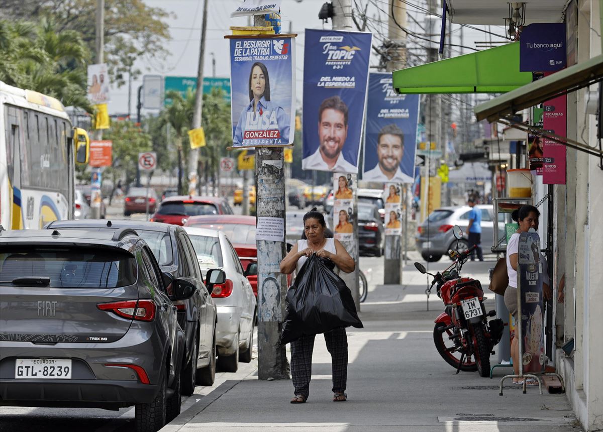 Una mujer camina por una calle de Guayaquil repleta de carteles. Foto: EFE