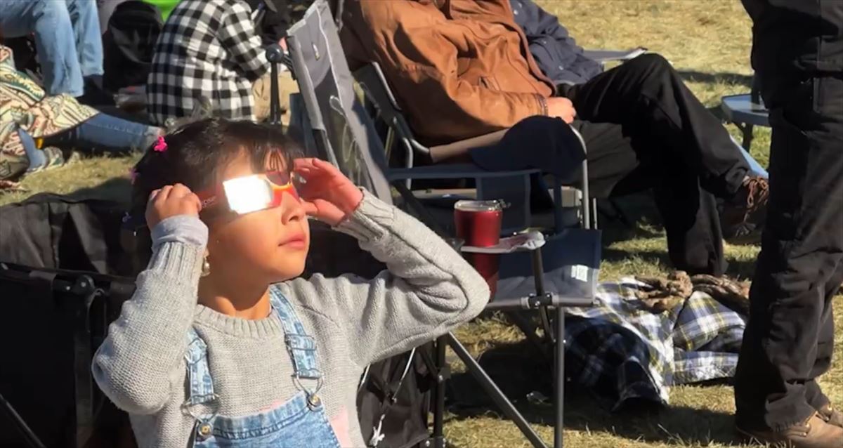 Una niña observa, debidamente protegida, un eclipse de sol. 