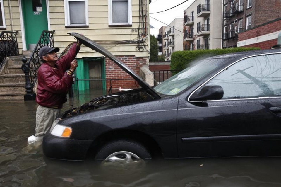 Un hombre intenta reparar su coche con la calle totalmente inundada. (Foto: EFE)