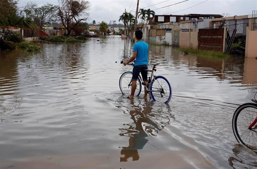 Un joven cruza en bicicleta una calle inundada. Foto: EFE