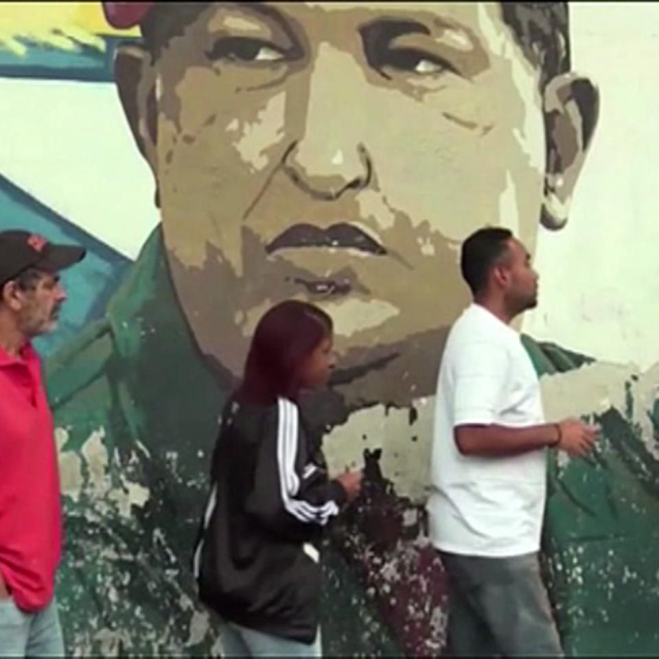 Varios venezolanos aguardan en fila delante una pintura de Nicolás Maduro.
