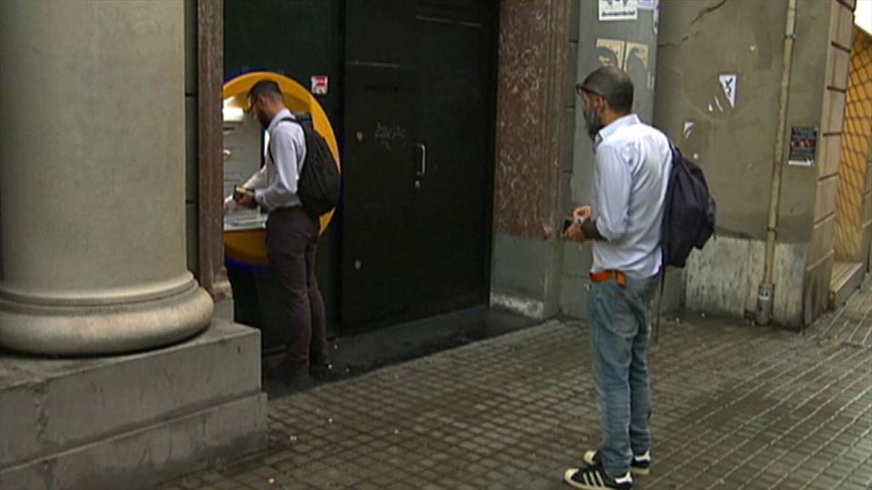 Un hombre espera su turno mientras otro retira dinero de un cajero.