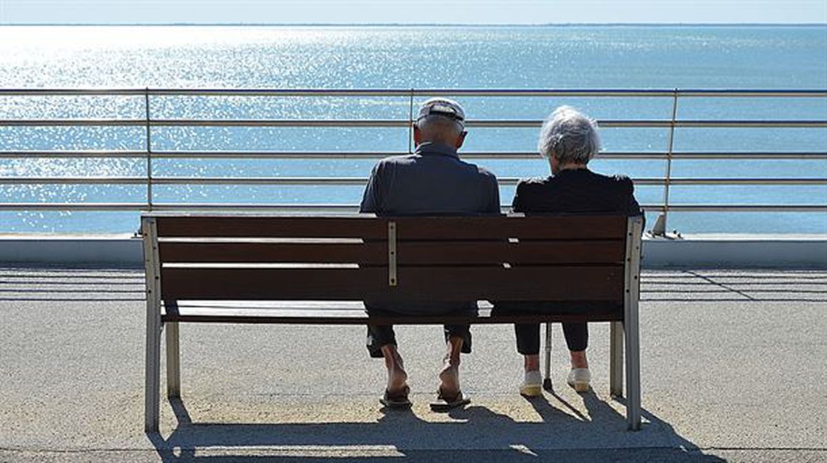 Dos personas mayores sentadas en un banco frente al mar