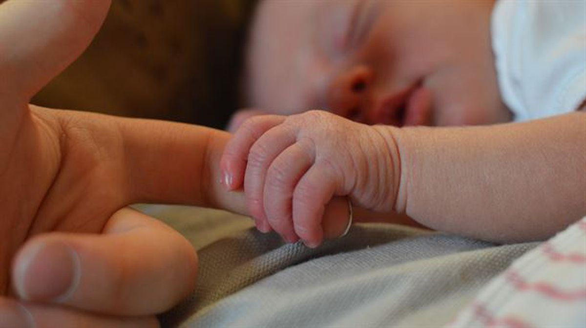 Un bebé agarra el dedo un adulto. 