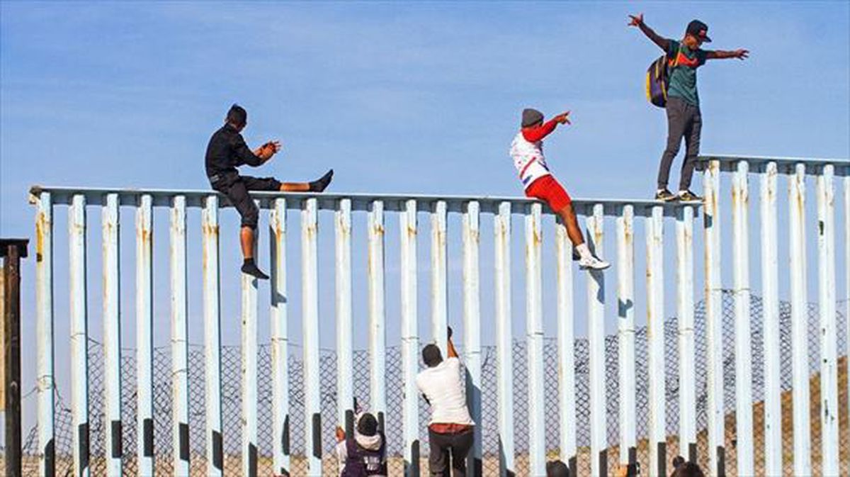 Varias personas subidas a la valla de la frontera entre México y EE. UU., en Tijuana