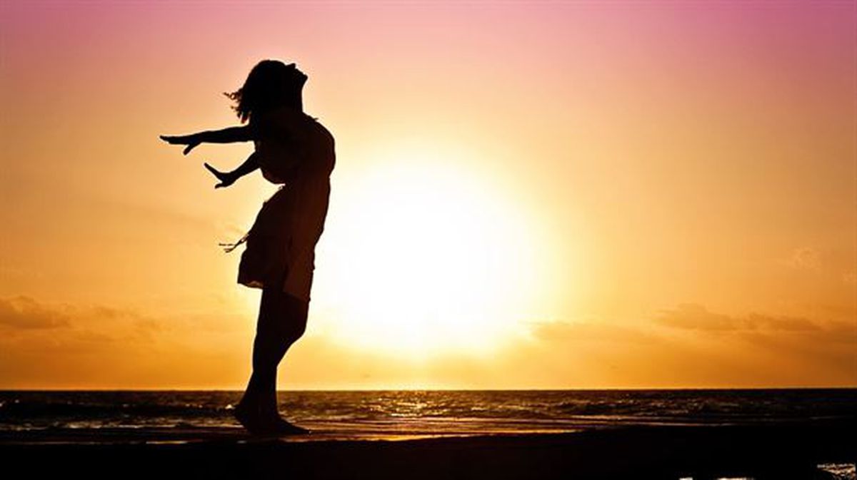 Una mujer con los brazos abierto disfruta del amanecer en la playa