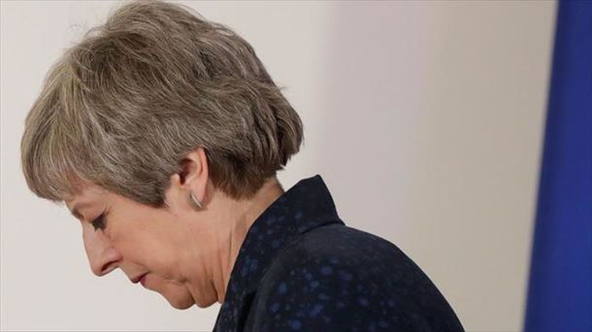 Theresa May, cabizbaja, con una bandera de la UE al fondo