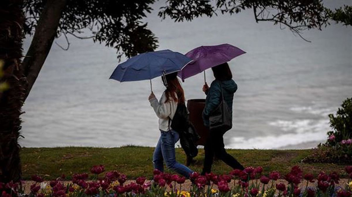 Varias personas se resguardan de la lluvia bajo sus paraguas en Bilbao. 
