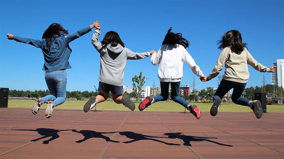 Adolescentes de espaldas saltando de la mano