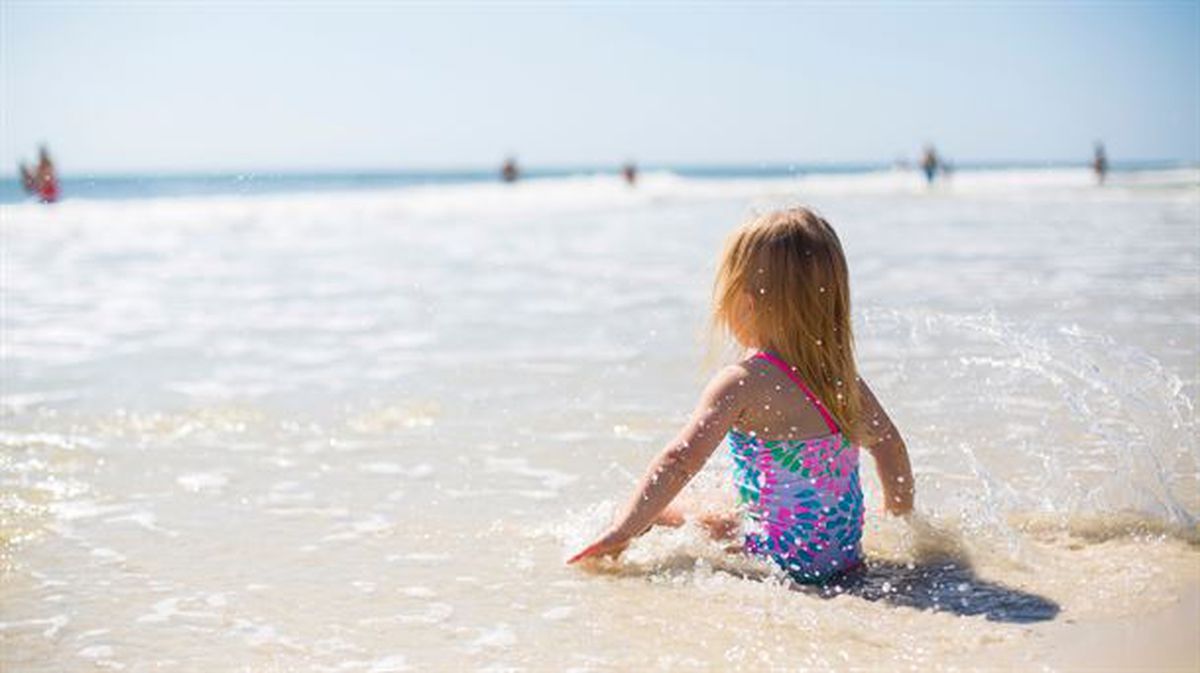 Una niña sentada de espaldas en la orilla de una playa