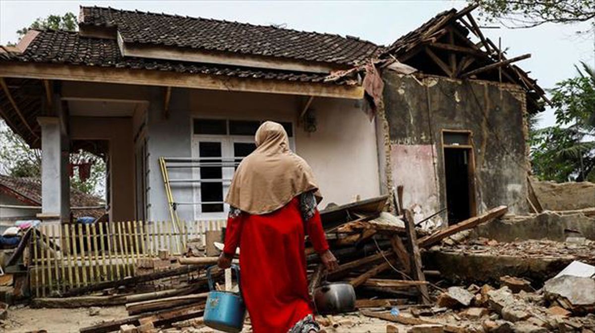 Una mujer frente a una casa destruida por el terremoto