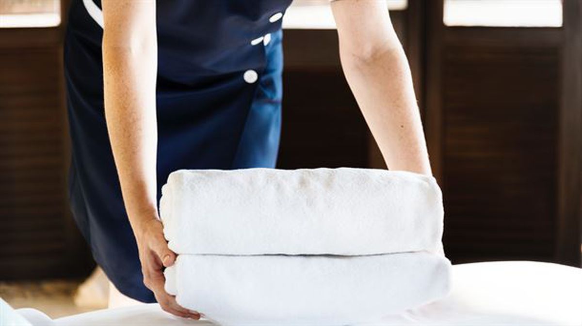Una camarera de hotel deposita toallas sobre una cama