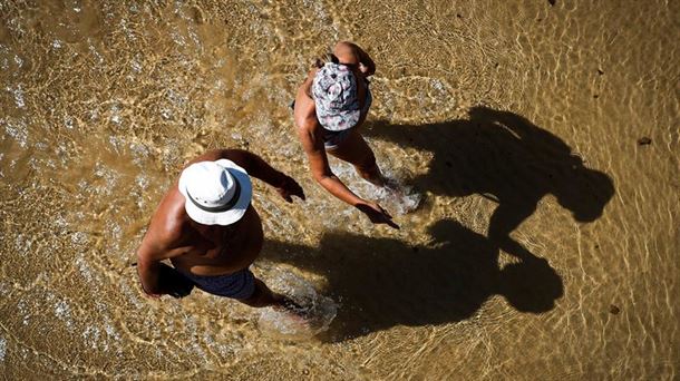 Imagen de una playa y dos personas caminando.