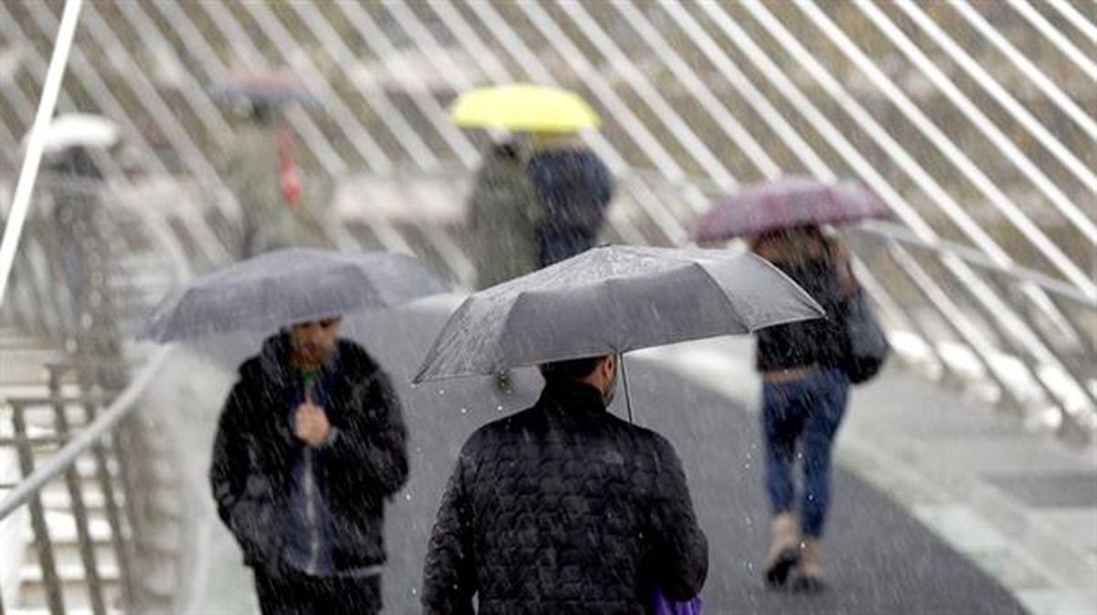 Varias personas se resguardan de la lluvia bajo sus paraguas en Bilbao. Foto: EFE