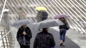 Varias personas se resguardan de la lluvia bajo sus paraguas en Bilbao. Foto: EFE
