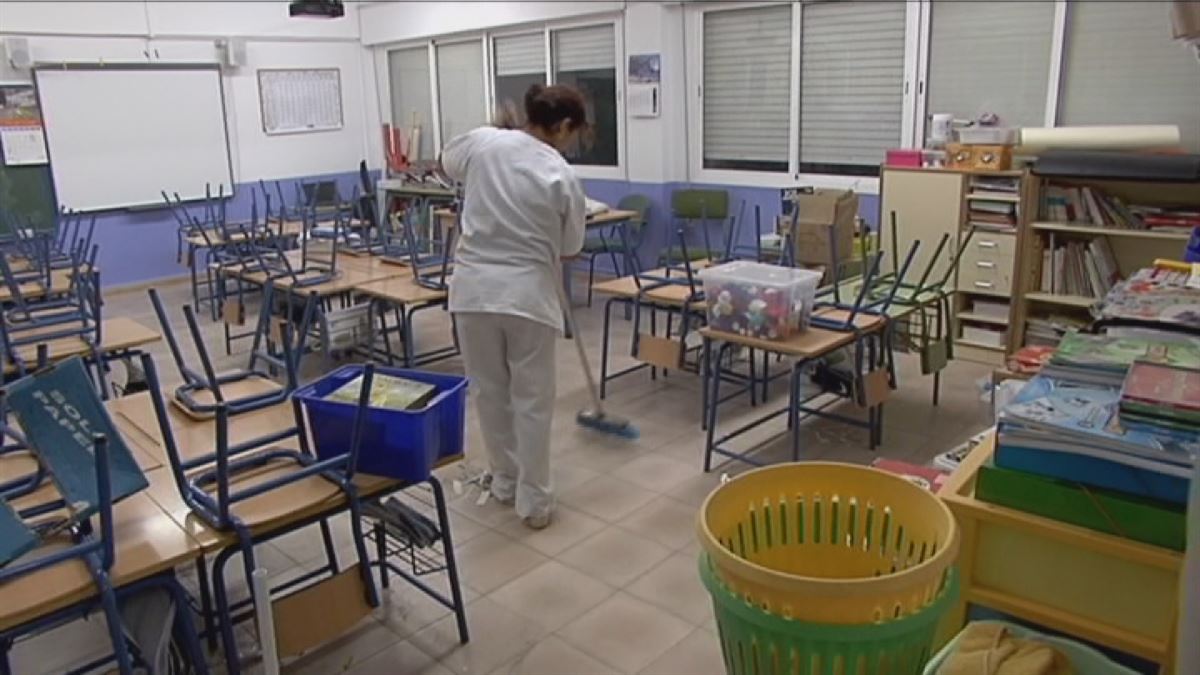 Una mujer limpia una clase de un centro escolar.