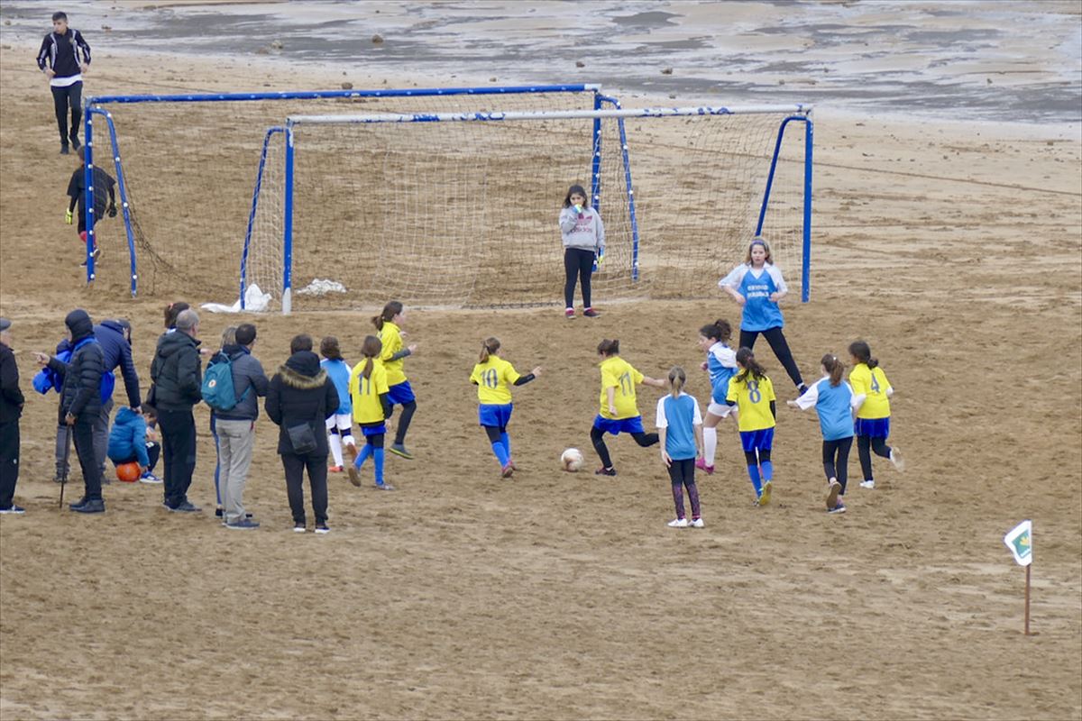 Un gupo de niñas jugando a fútbol en una playa.