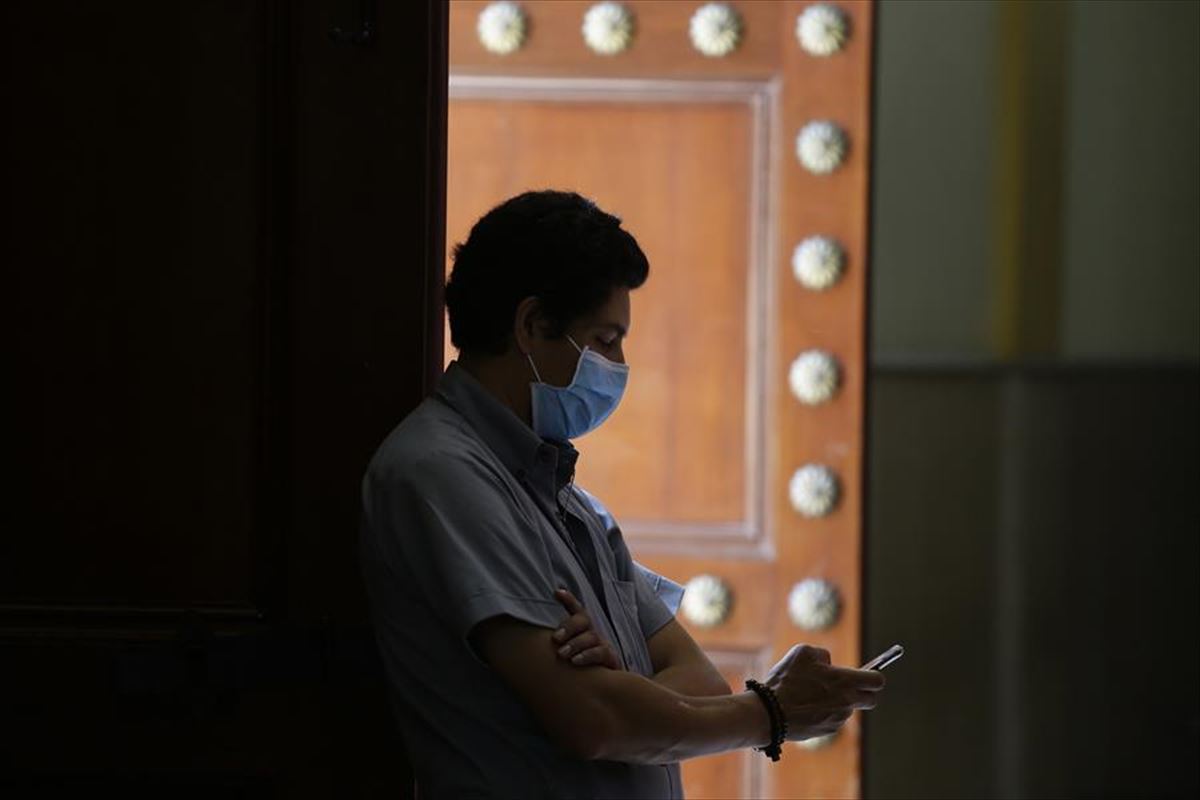 Un hombre observa su teléfono móvil con una mascarilla como medida contra el coronavirus.