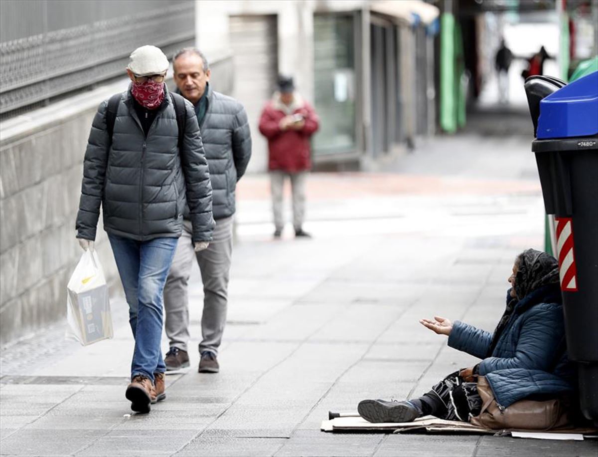 Una mujer sin techo pide en la calle frente a un ciudadano protegido con guantes y pañuelo.