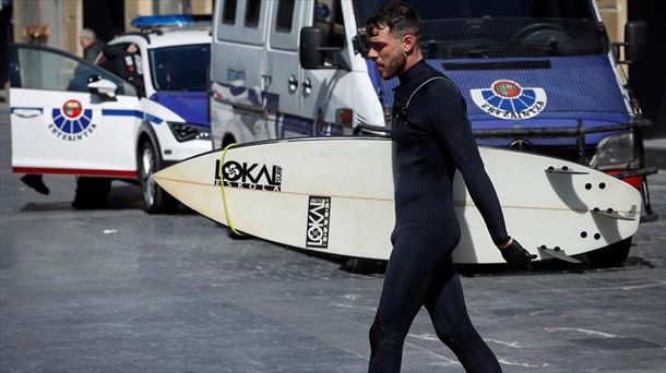 Un surfista pasa por delante de un patrulla de la Ertzaintza en Donostia.