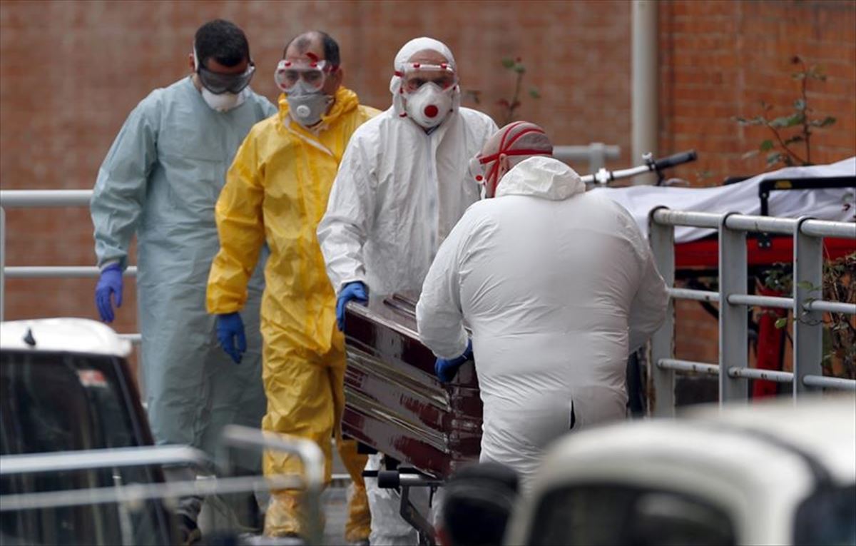 Trabajadores de una funeraria protegidos, trasladan de una morgue a un fallecido por coronavirus.