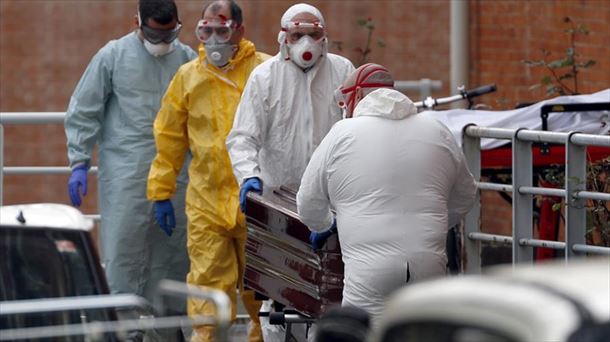 Trabajadores de una funeraria protegidos, trasladan de una morgue a un fallecido por coronavirus.