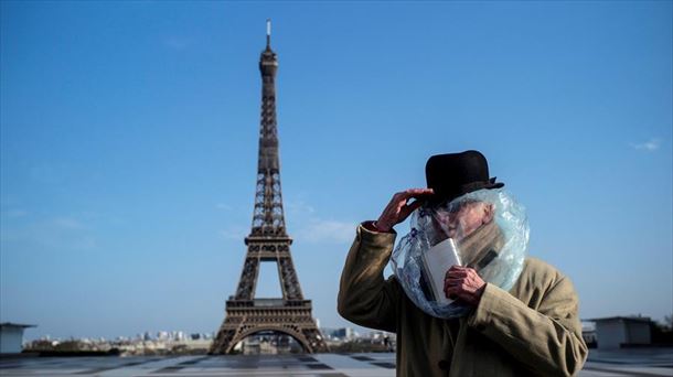 Gizon bat Parisko Eiffel dorrearen aurrean, burua plastiko batekin estalita.