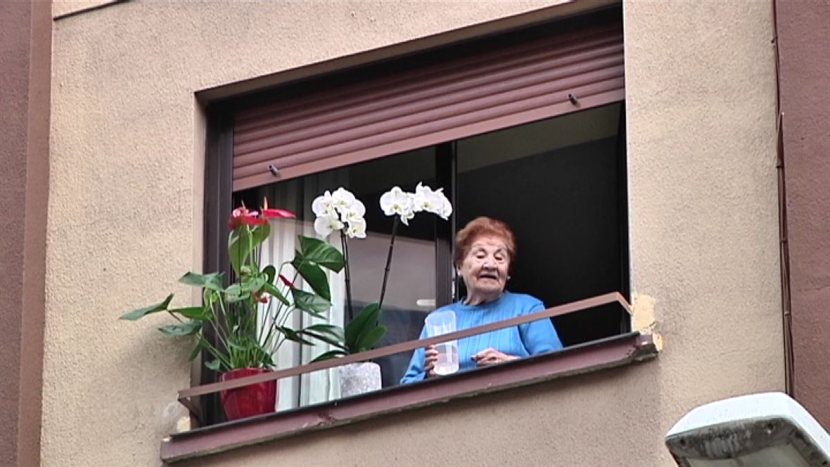 Una mujer mayor se asoma por la ventana de su casa.