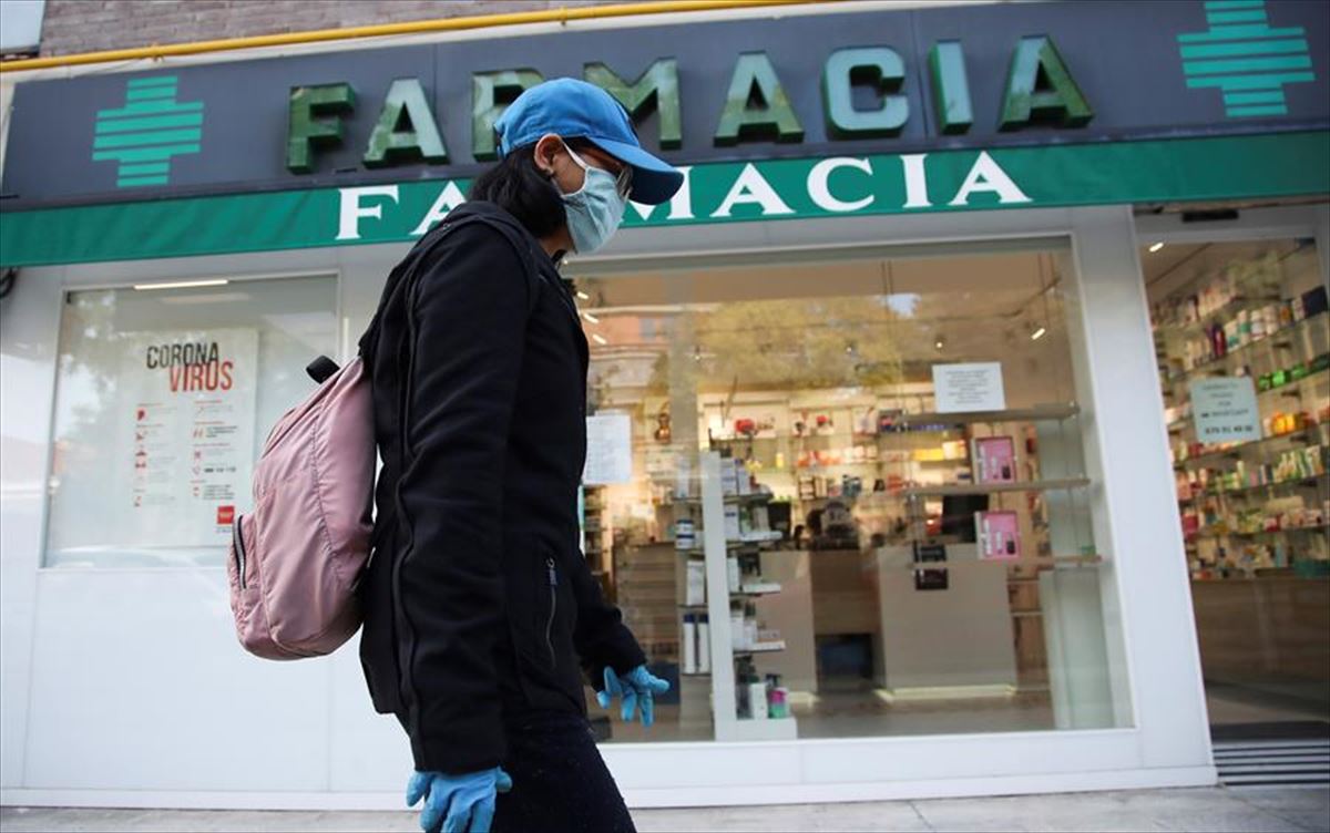Una persona con máscara pasa frente a una farmacia. Foto: Efe