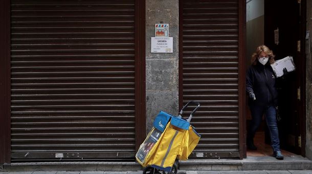 Una cartera de Correos con mascarilla saliendo de un portal.