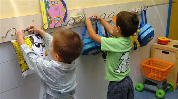 Dos niños colgando sus mochilas en las perchas de la escuela infantil