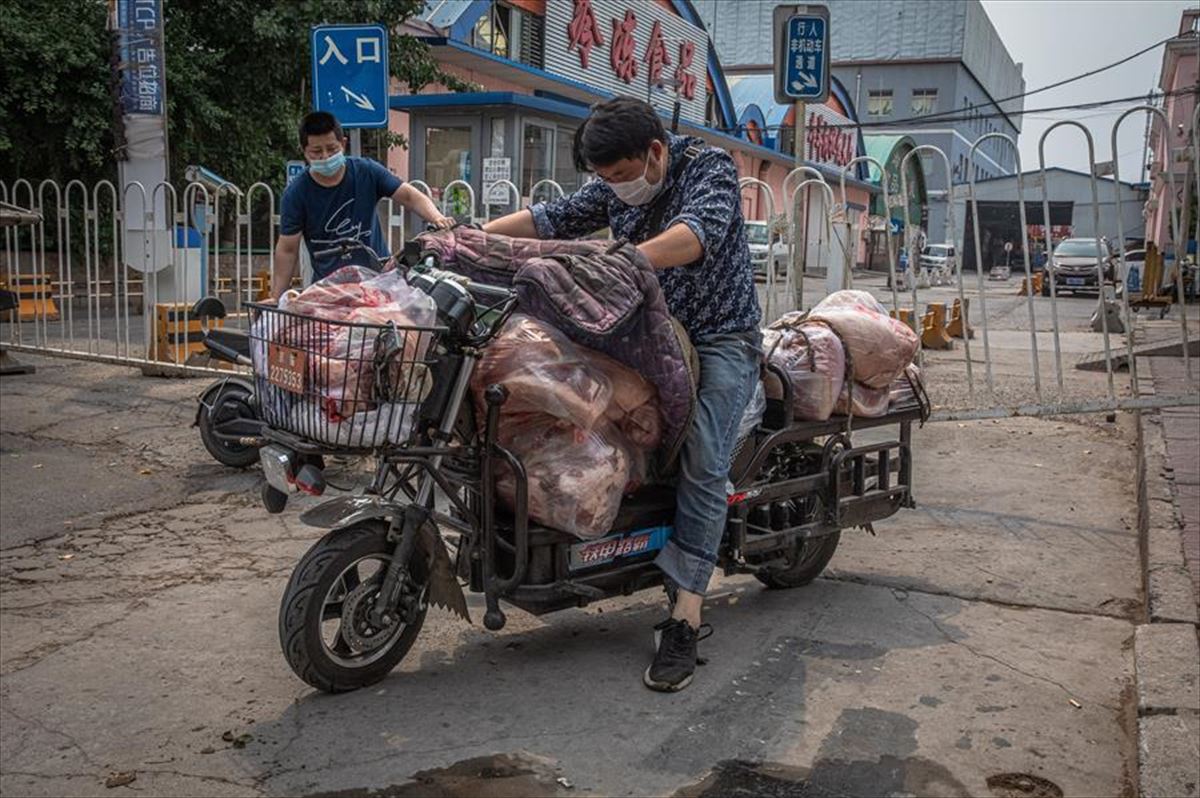 Hombres con máscaras cargan un scooter con carne al lado del edificio cerrado del mercado Xinfadi