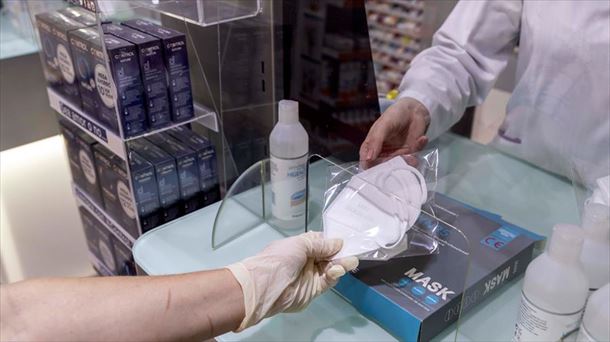 Una persona adquiere una mascarilla quirúrgia en una farmacia.