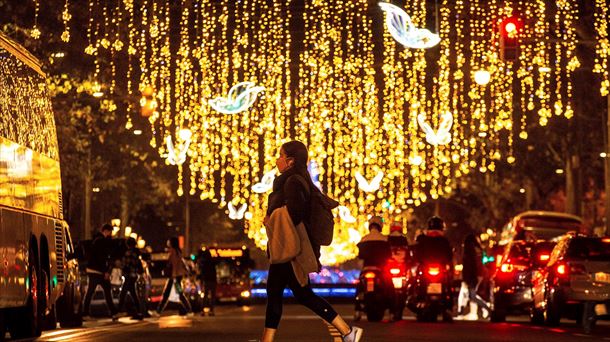 Una mujer, con mascarilla, camina por una calle adornada con luces navideñas.