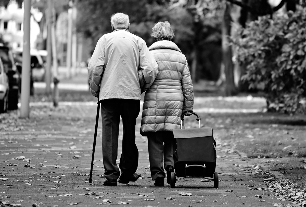 Dos personas mayores pasean juntos por la calle. 