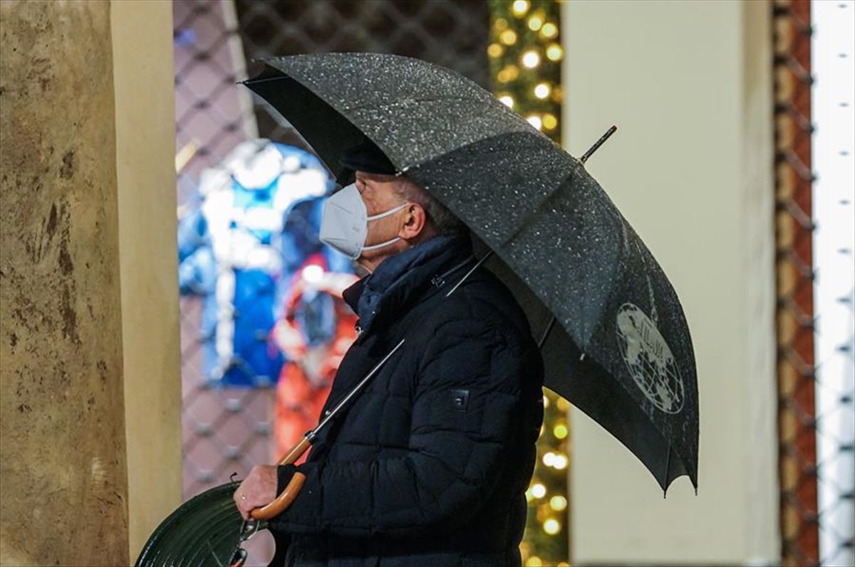 Un hombre con mascarilla bajo un paraguas