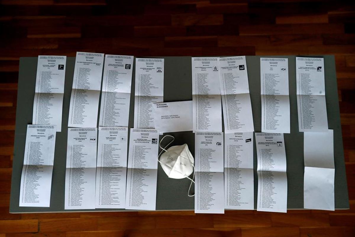 Papeletas de las 15 candidaturas a las elecciones 14F, junto a una mascarilla.