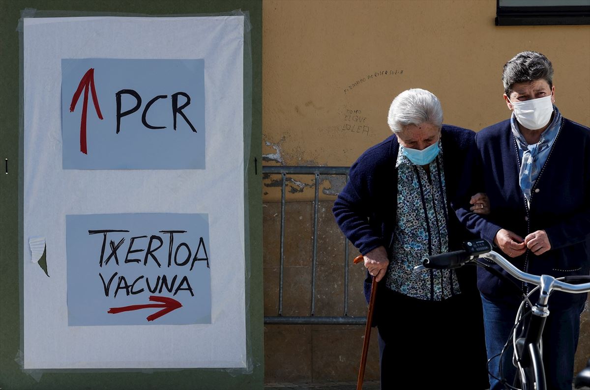 Un par de mujeres pasan cerca de un cartel indicativo de PCR y Vacunación en Lazkao