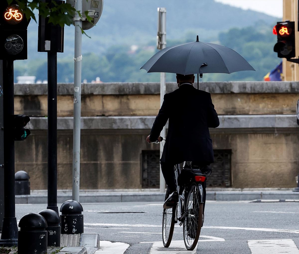Una persona en bicicleta con paraguas bajo la lluvia en San Sebastián
