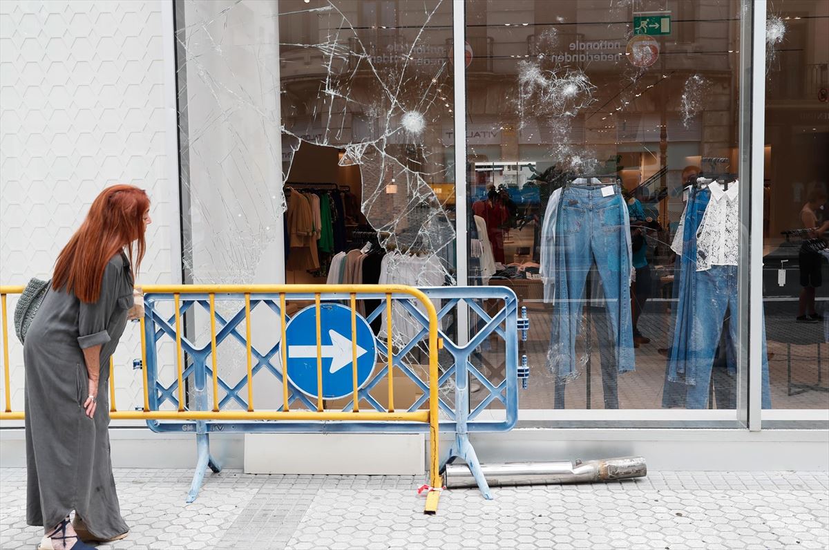 Una mujer observa un escaparate roto durante los incidentes en San Sebastián. Foto: EFE