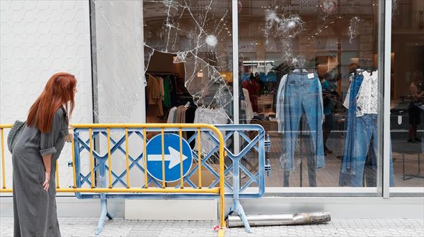 Una mujer observa un escaparate roto durante los incidentes en San Sebastián. Foto: EFE