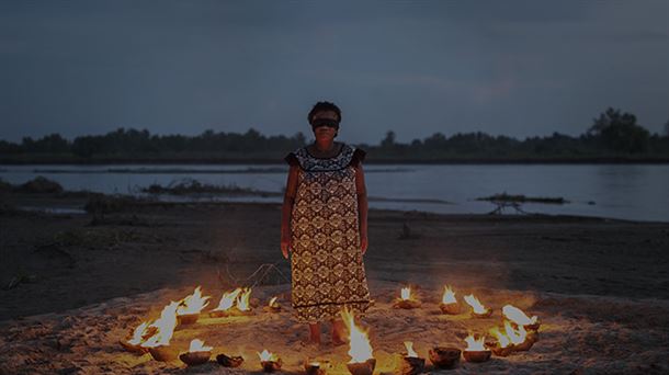  mujer, vestida con ropa tradicional africana.ojos vendados, parada dentro de un círculo de fuego