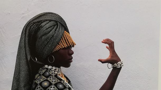 Mujer africana con una de sus manos en forma de garra, dirigida hacia su cara.