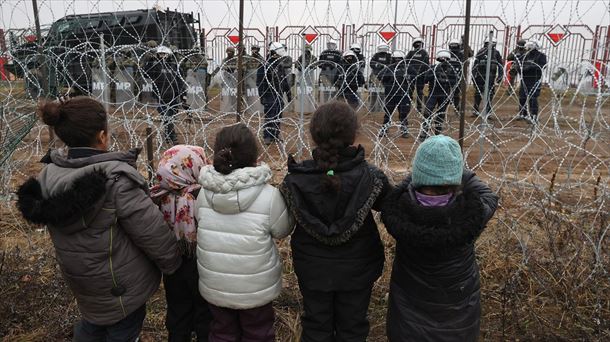 Menores migrantes observan a los policías polacos que vigilan la frontera. Foto: EFE