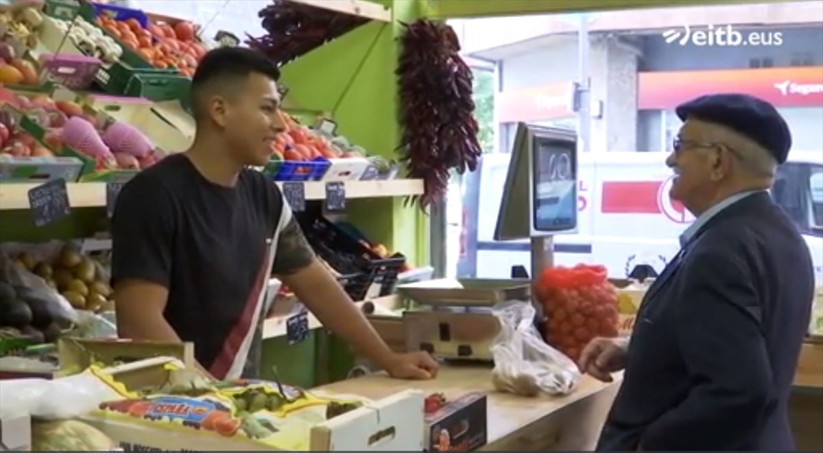 Un chico y y un señor, charlan en una frutería. Imagen extraída de un vídeo de EITB. 